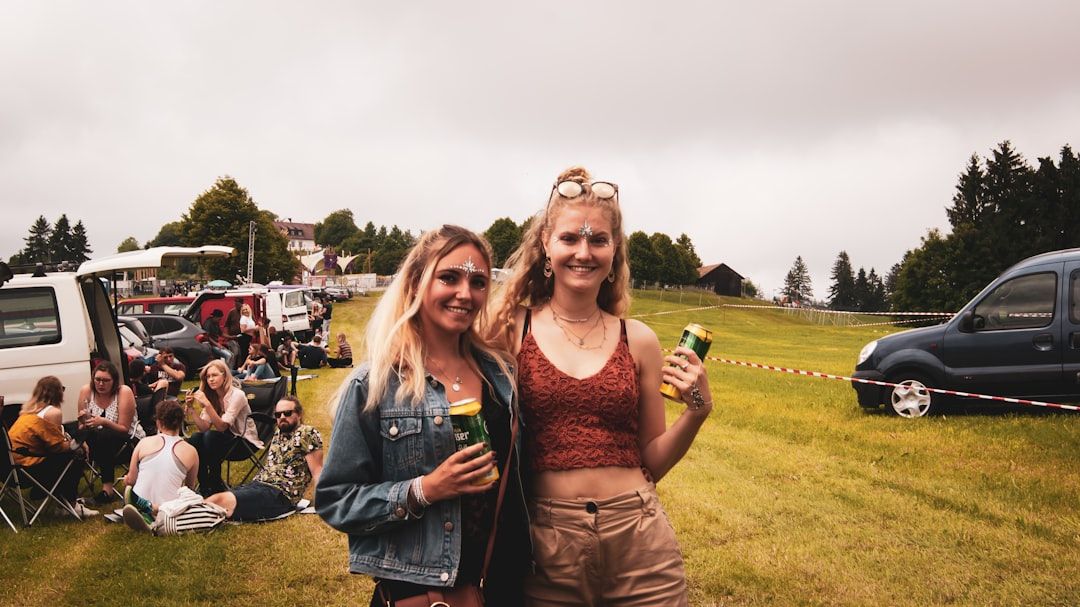 Twee glimlachende festivalbezoekers met blikjes drank op een festivalterrein.