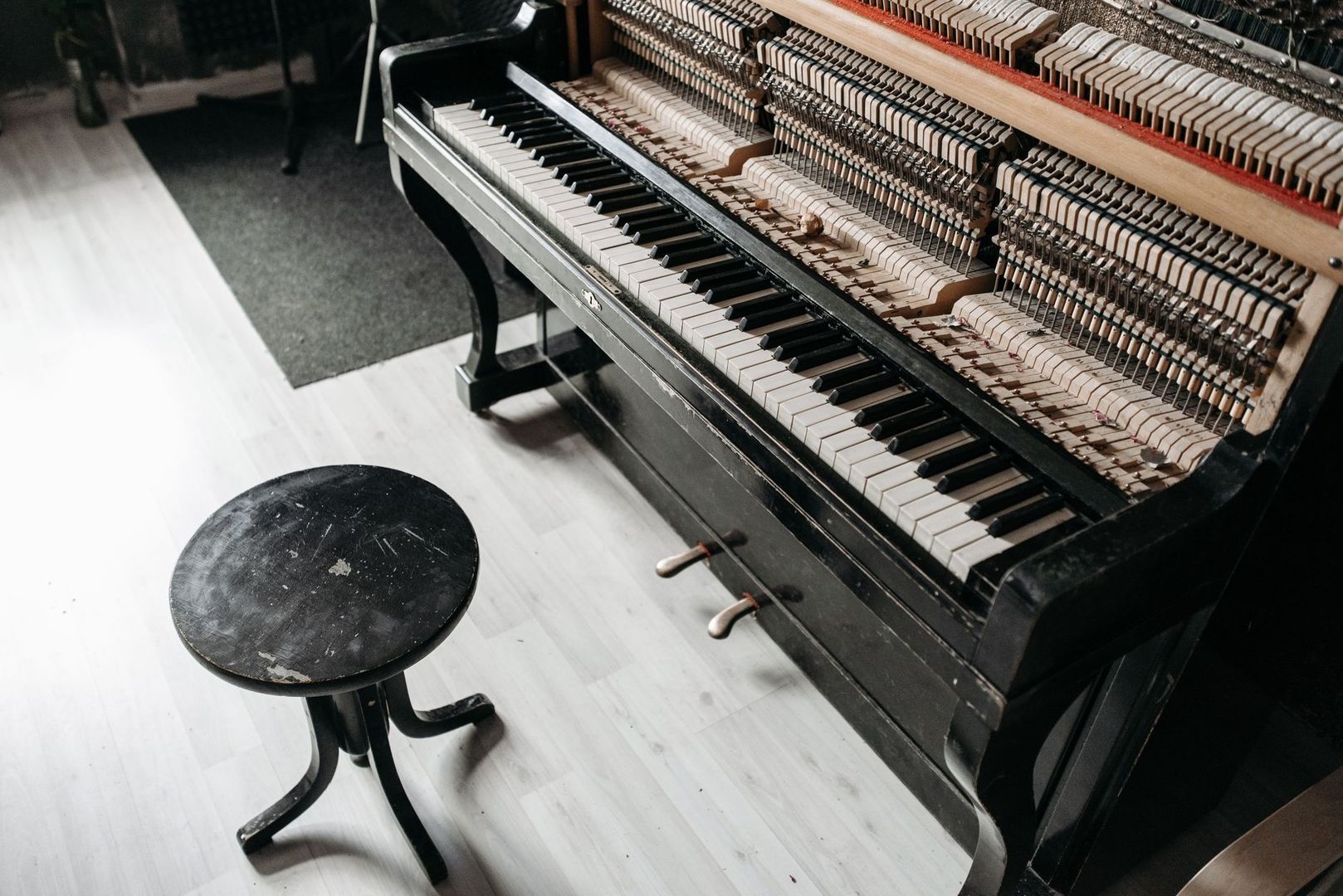 Open piano met zichtbare hamers, toetsen en twee pedalen naast een pianokruk