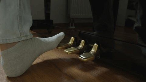 Voet in een sok boven de drie messingkleurige pianopedalen
